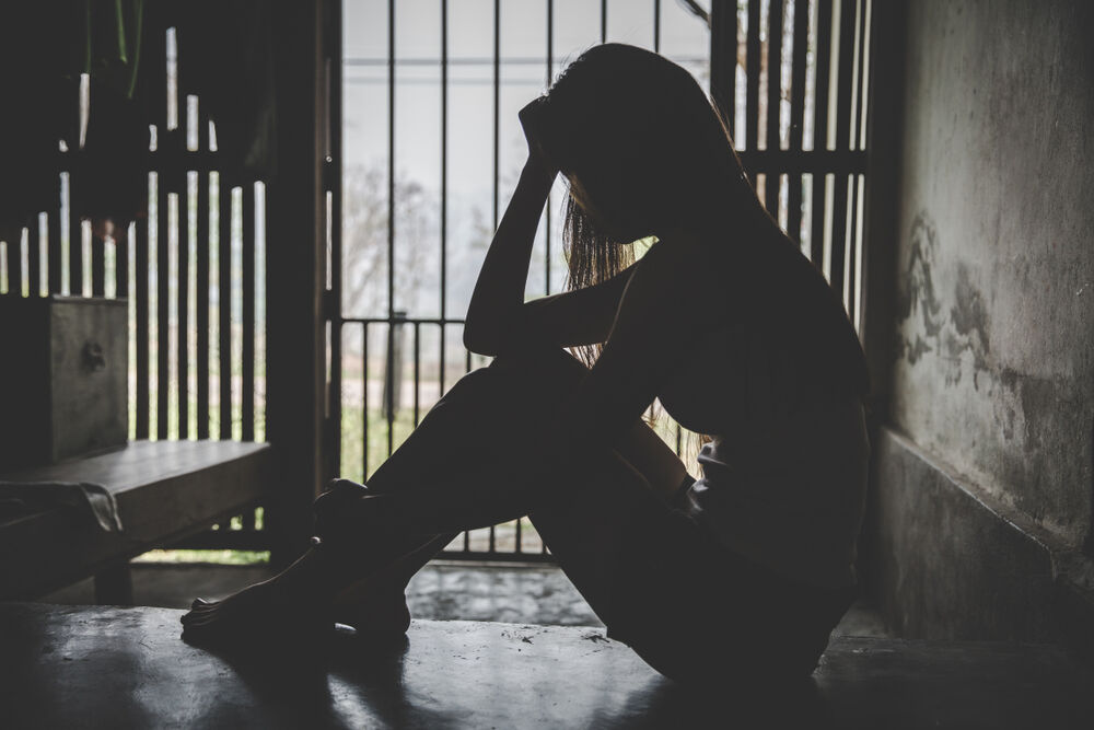 Woman's silhouette sitting down against a barred window