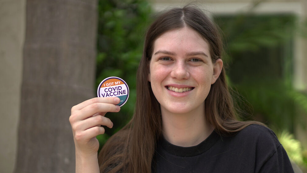 16-year-old girl holds up COVID-19 vaccine sticker