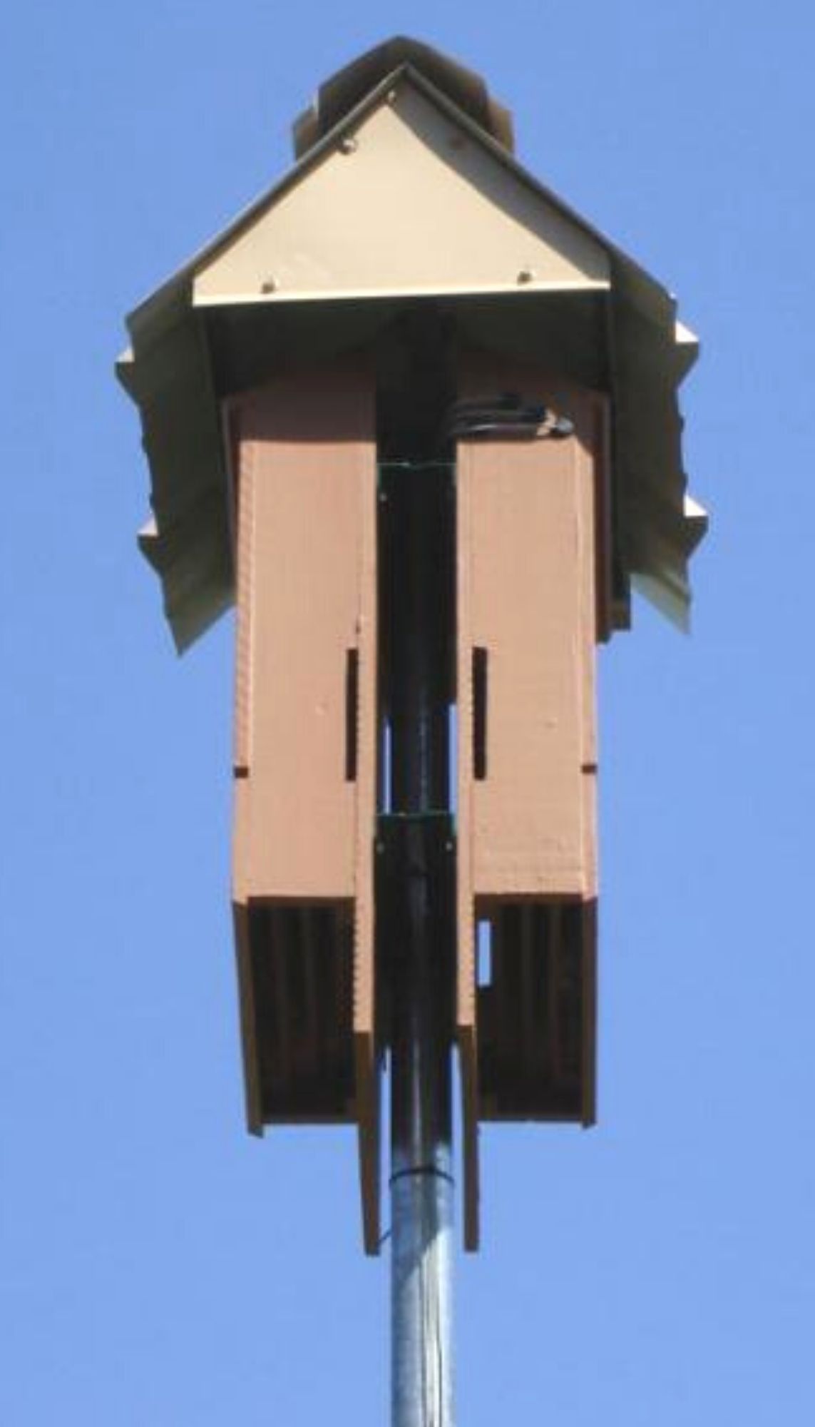 Two four-chamber bat houses mounted back-to-back on a pole and covered with a metal roof