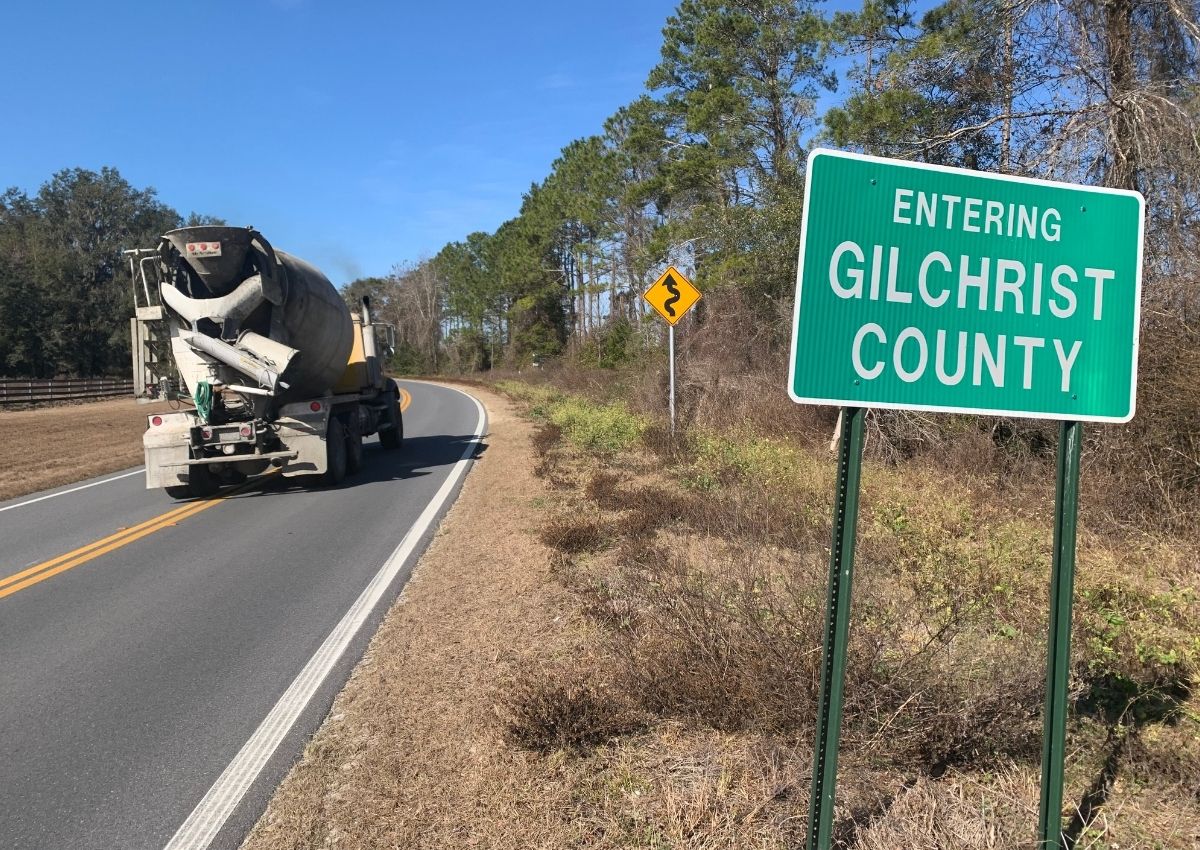 Cement truck driving past Gilchrist County sign on County Road 232