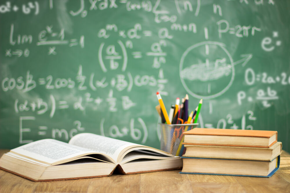 Classroom concept with books, pencils on table in front of chalk board