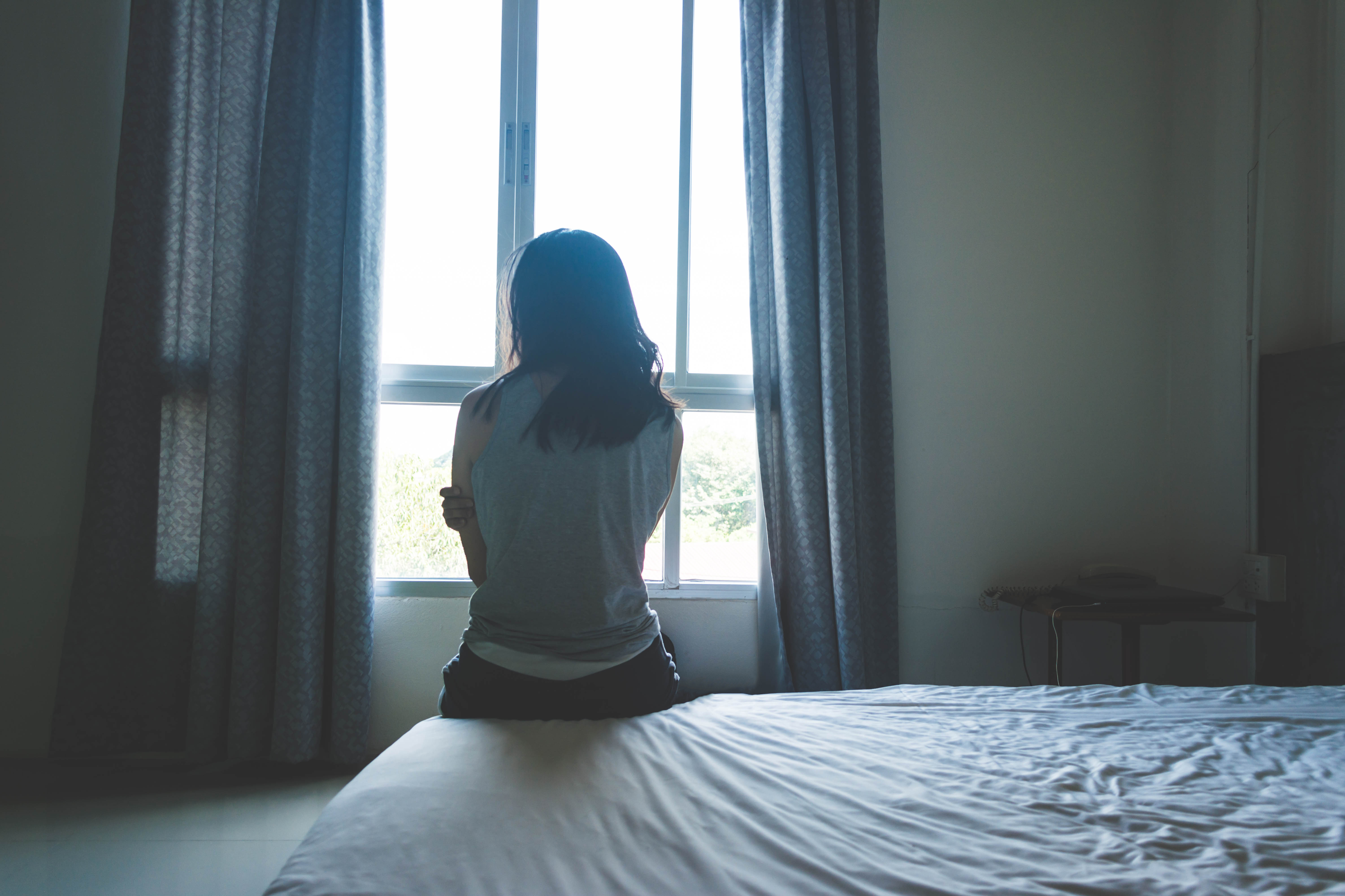 woman sitting on the edge of her bed looking out the window