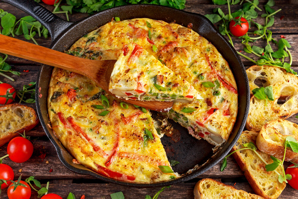 Frittata with eggs, bacon and red peppers on wooden table