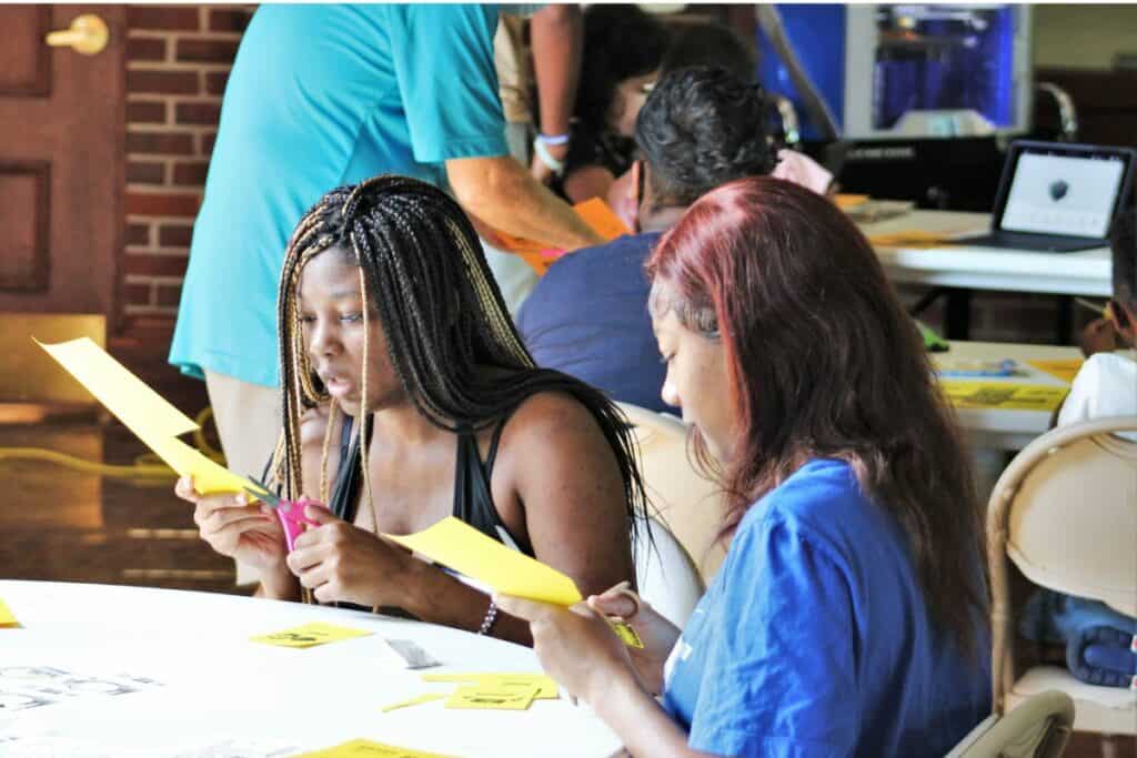 New Tech Now event attendees cut out paper cubes that they will soon turn virtual.