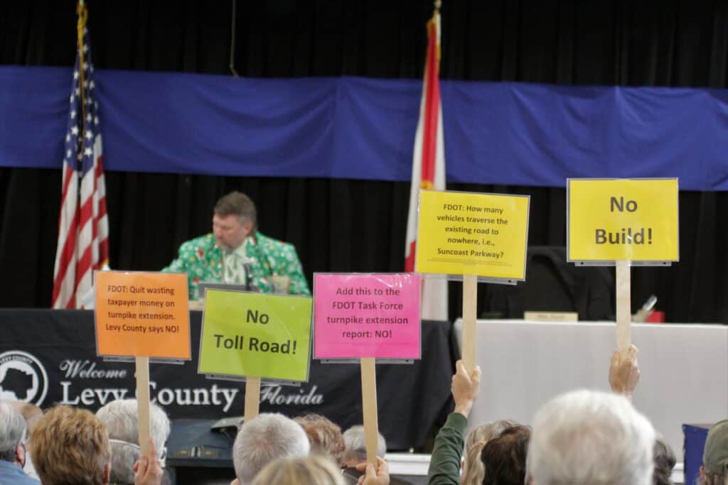 Residents hold No Build signs during a Levy County Commission meeting in December 2021 with Chair John Meeks sitting on the dias.