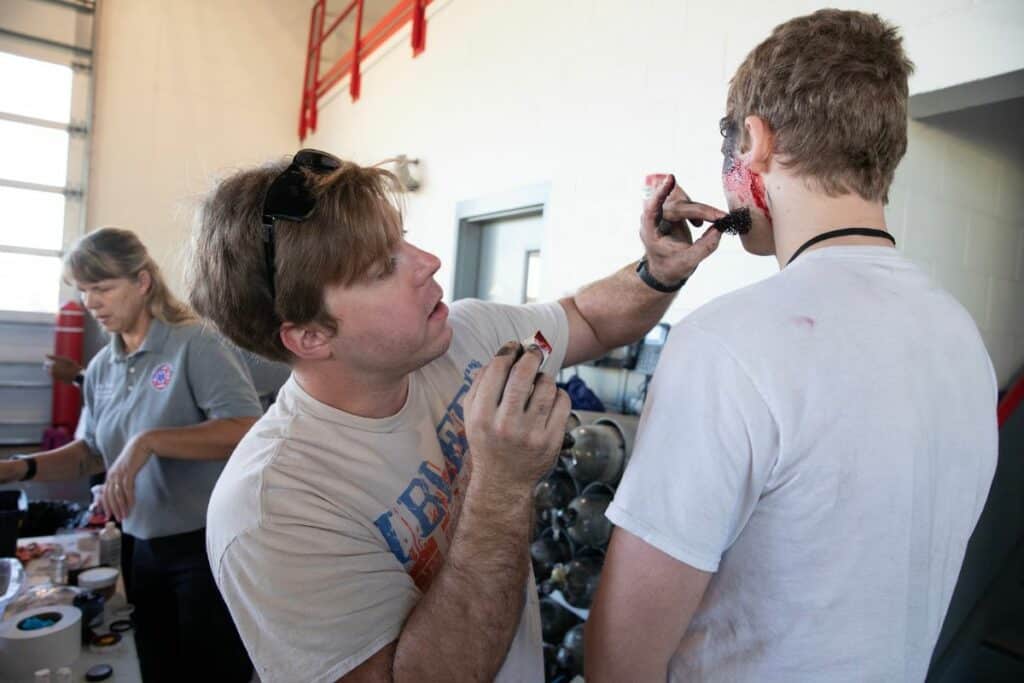 Brandon Friend, an Alachua County Fire Rescue firefighter trainee, applies make-up to Joel Burgett's face to simulate a contusion to the Santa Fe Community College student's left temple.