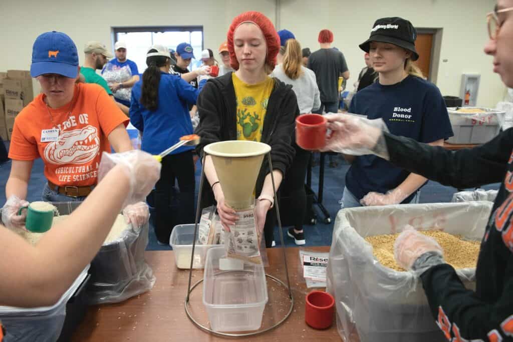 UF Biology major Alexis Dvorak, center, steadies a bag beneath a funnel so fellow volunteers can add rice, dried soy, dehydrated vegetables and a nutritional supplement packet to it.