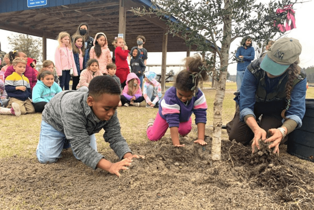 Alachua County arborist Lacy Holtzworth helps Greenfield Preschool students plant trees at Easton Newberry Sports Complex.