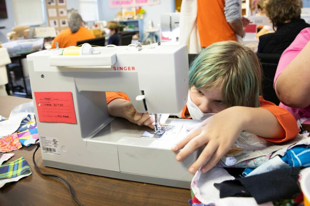 Charlotte McVicar, 11, threads her sewing machine's bobbin. Charlotte volunteered with her parents, Brittany Spaulding and James Spaulding and her cousin, Miles Watson, 8.