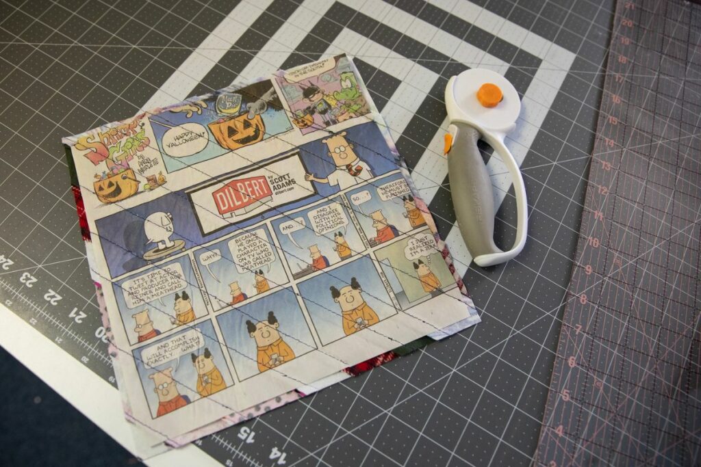 Strips of fabric are quilted to squares of newspaper as a way to ensure each quilt square is of equal size.