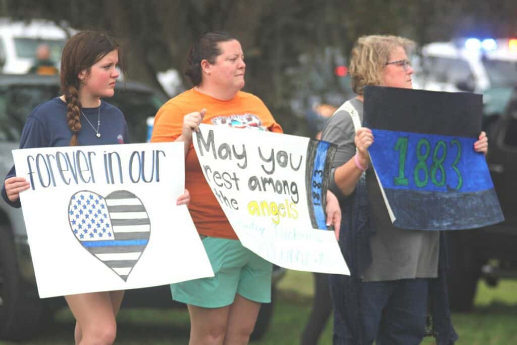 People holding signs honoring Alachua County Sheriff's deputy Nikolas Tilliman during a procession bringing him to the Milam Funeral Home in Newberry on Friday.