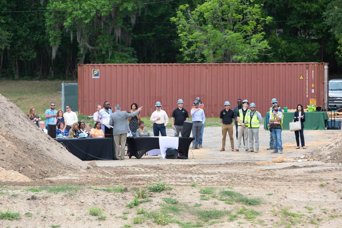 Scorpio President Domenic Scorpio, in gray jacket, gestures toward the construction site as workers raise the wall.
