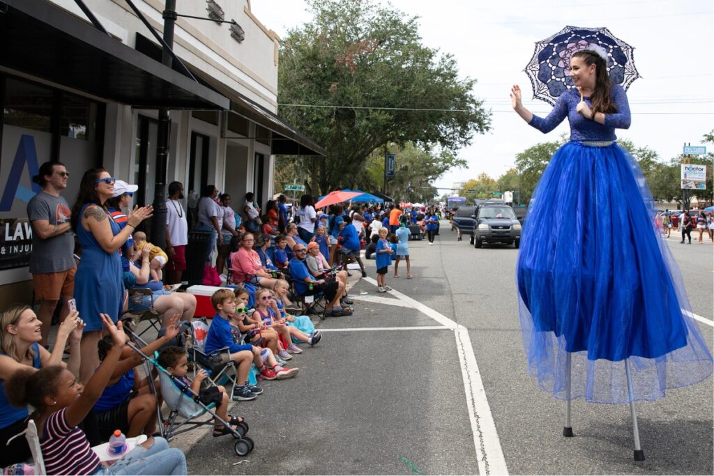 A lady walking on stilts waves to the crowd at the UF Homecoming Parade on Friday.