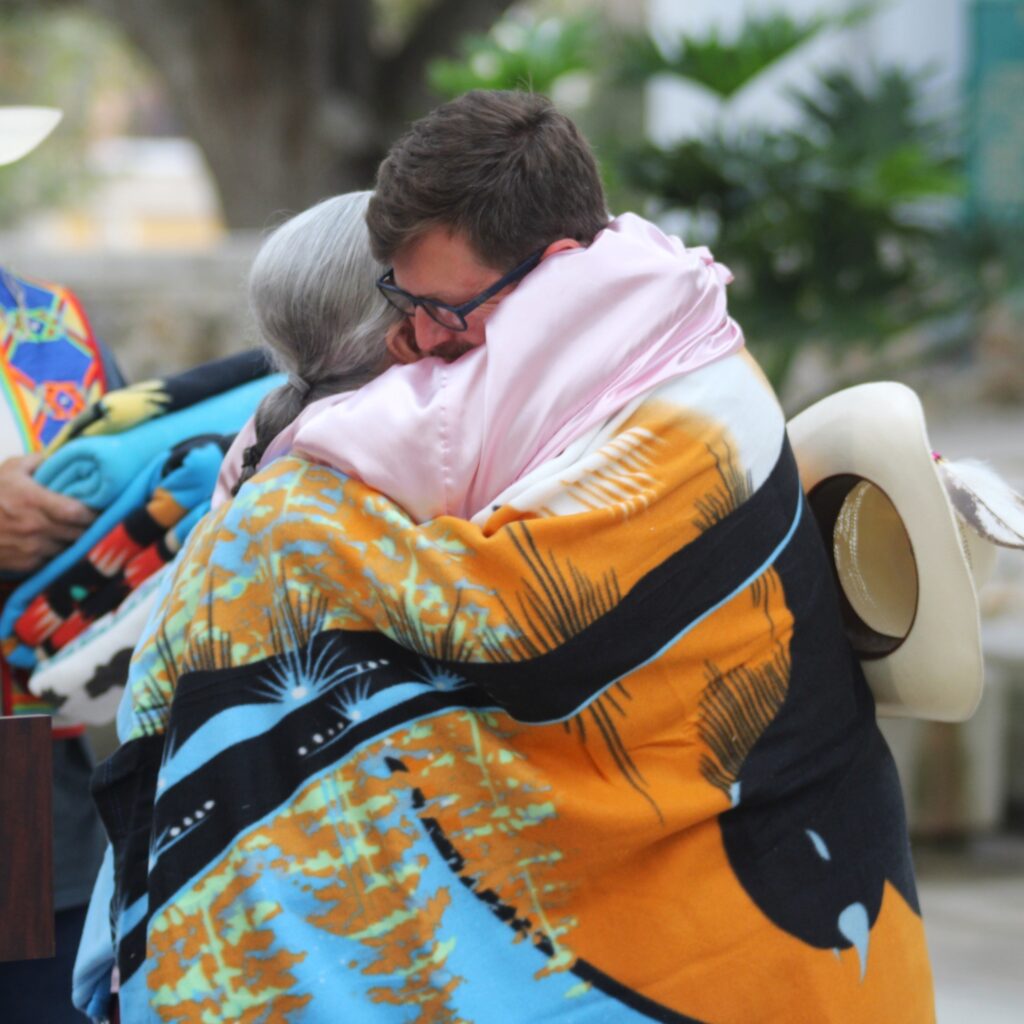 Former Mayor Lauren Poe and Maria Whitehorse hug after she gives him a gift.