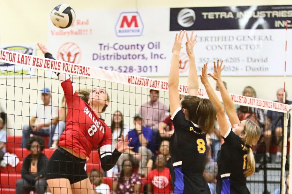 Williston's Grace Dola with a hit against Newberry's Sarah Watson (8) and McKenzie Moses (12) on Tuesday.