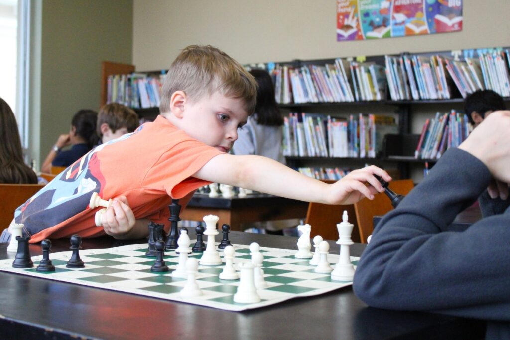 Levi Merkel, a junior kindergartener, reaches to place his queen deep in white's territory during a practice match at the Oak Hall Chess Club.