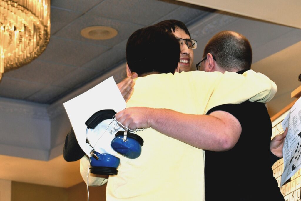 Finalists David Plotkin, Paolo Pasco and Will Nediger hug after completing the championship round of the American Crossword Puzzle Tournament.
