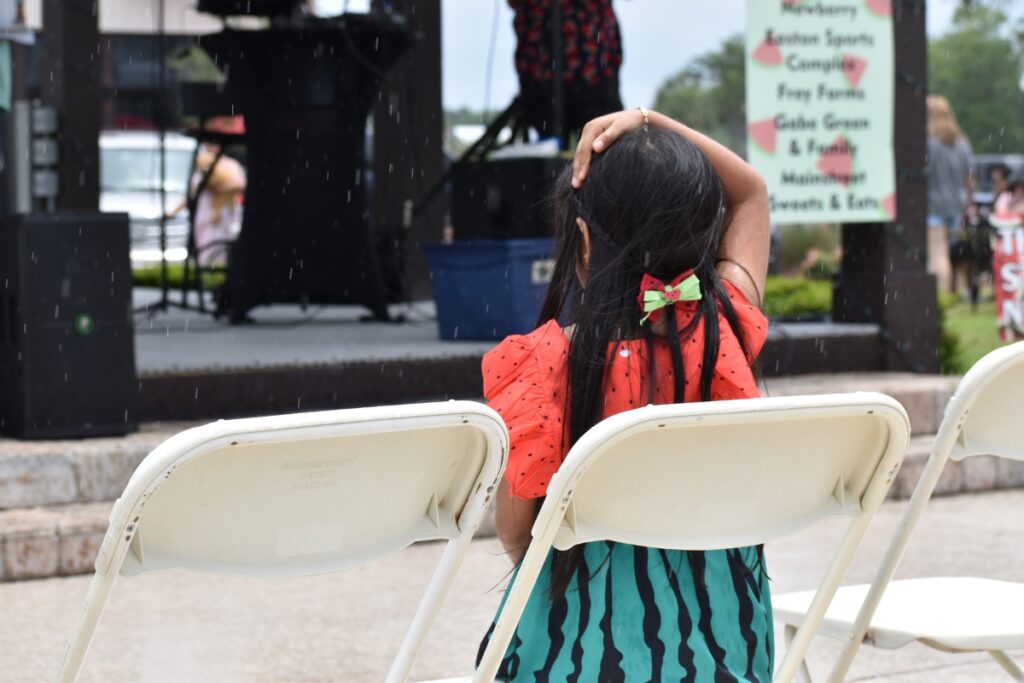 Alexa Lagunas keeps her seat through the rain to watch her sister Sheriyn in the Watermelon Queen pageant.