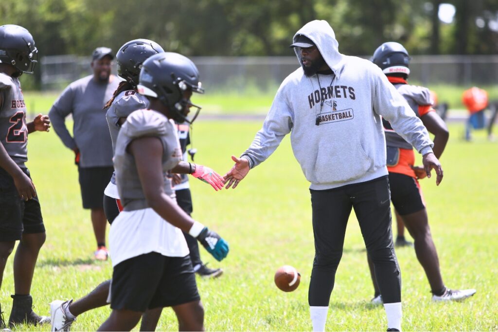 Hawthorne football coach Cornelius Ingram (hoodie) congratulates a player during practice on Wednesday. Ingram is entering his 10th season as head coach of the Hornets.