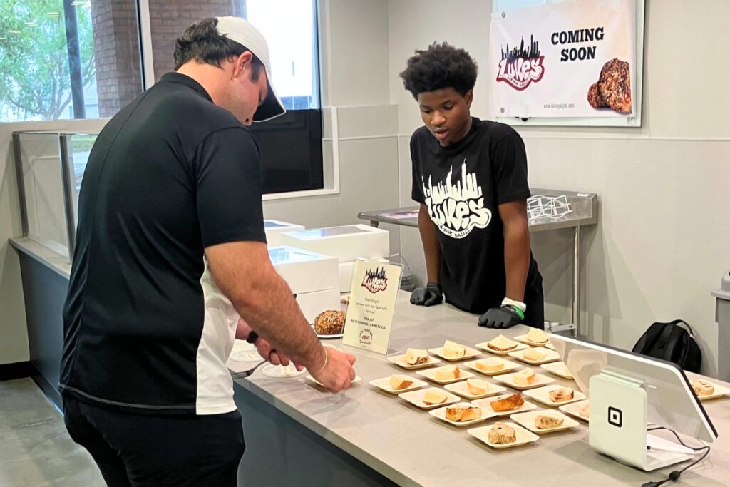 Josiah Hurst (right) serves Luke's NY Bagels samples at the local favorite's new food hall location.