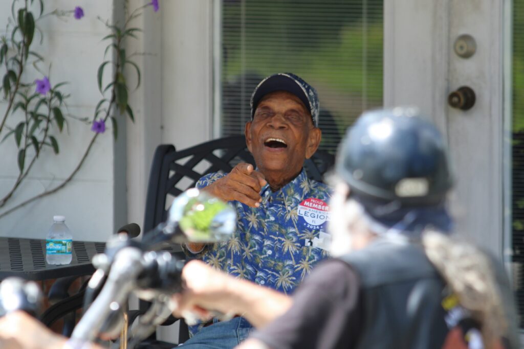 Joseph Williams points and waves to the American Legion members driving past his house.