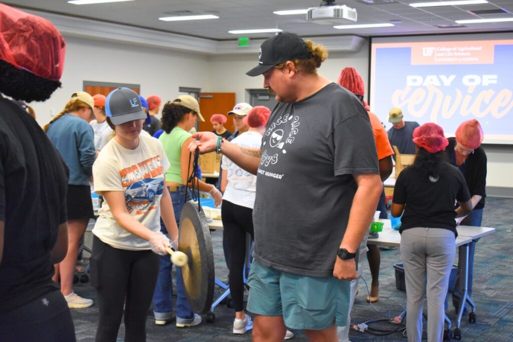 Chase Woodburn holds the gong while Carlie Griffin rings it for 8,000 meals packed on Thursday morning.