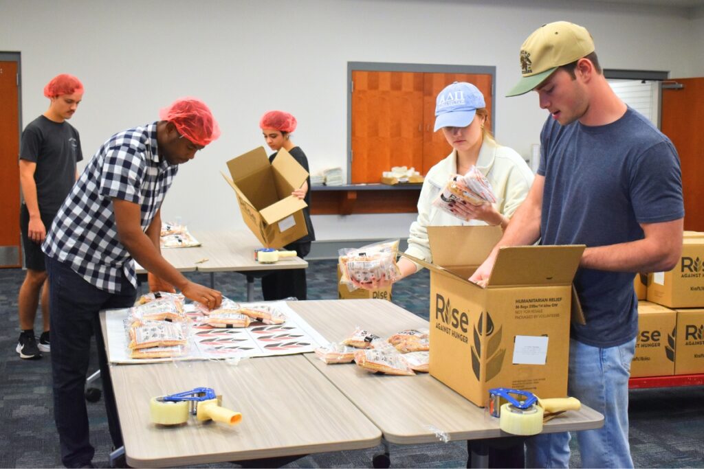 Emma Putnam (blue hat) hands packaged food to Robbie Belcher to box up.