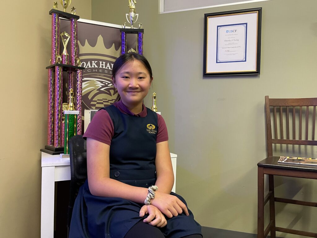 Sophie Li sits in front of a section of trophies earned by Oak Hall's female chess players. Photo by Seth Johnson