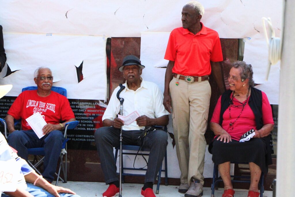 Former LHS coach Jesse Heard (second from left) and wife Yvonne (right) sit in the shade of the new memorial wall. Photo by Lillian Hamman