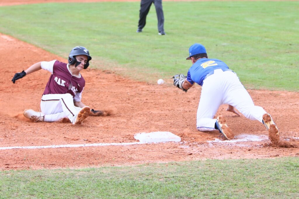 The ball gets past Newberry's Aiden Michaux (2) as Oak Hall's Brayden Farmer (22) slides safely to third base. Photo by C.J. Gish