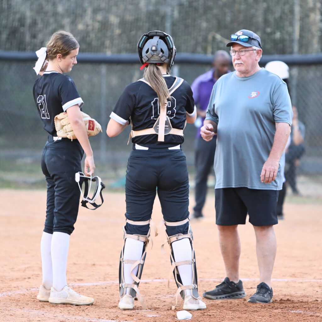 Santa Fe coach Gene Findley talks to pitcher Ryleigh Davis (21) and catcher Ainslea Kelsoe (18) in a game against Gainesville. Photo by C.J. Gish