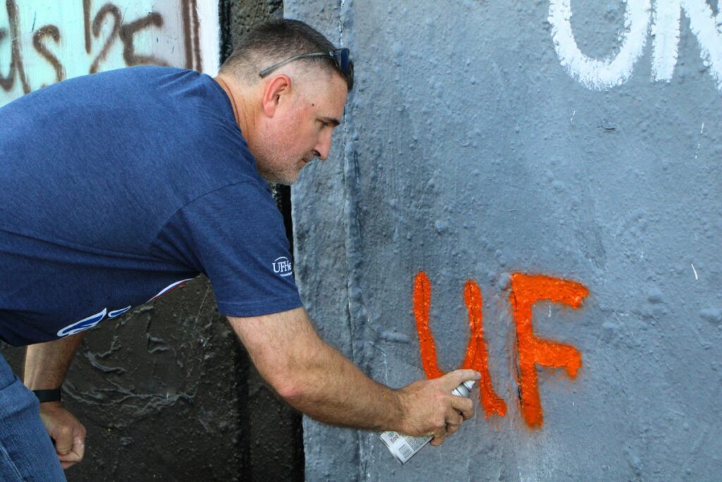 Joe Munson spray paints 'UF Health Psych' logo on mural. Photo by Lillian Hamman