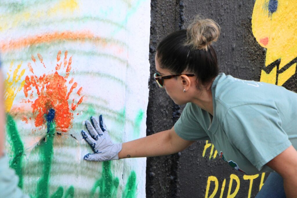 Mural organizer Jessica Yupanqui paints flowers out of handprints on the mural. Photo by Lillian Hamman