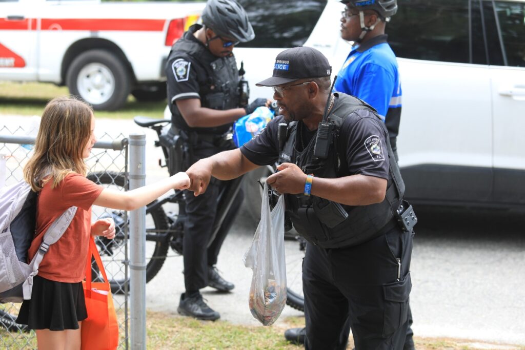 Officer Adrian Lumpkins greets students by name and hands out candy at the Bike, Roll, Walk to School event. 
