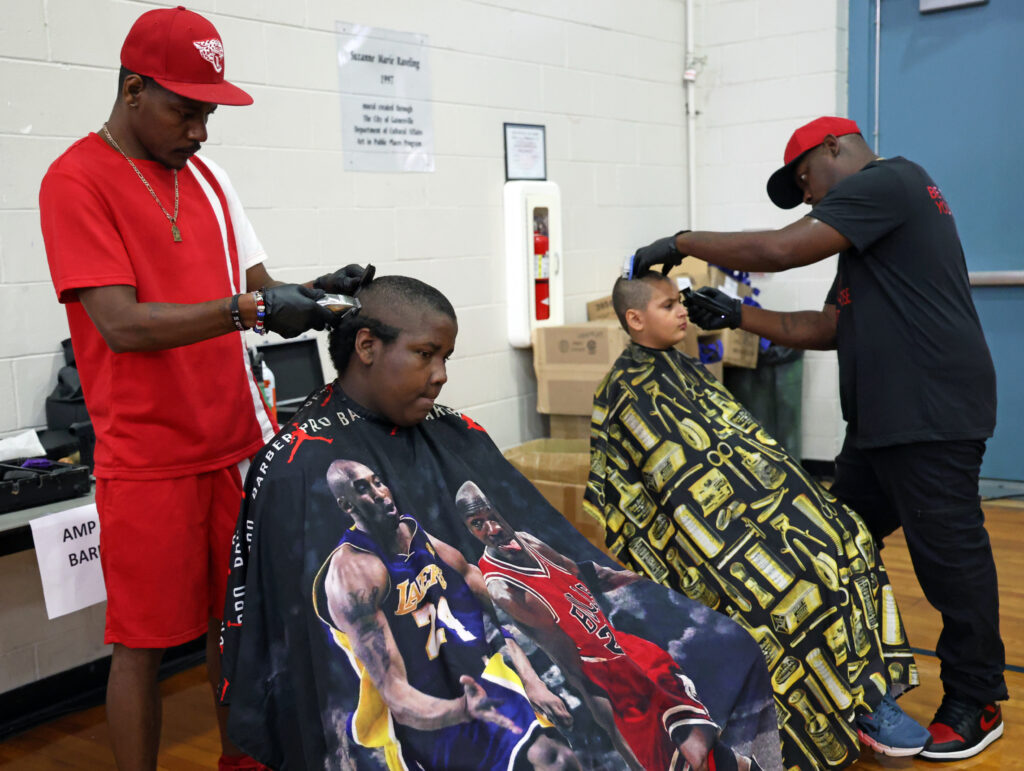 Anthony Anderson (left) cuts Bobby Fletcher's (second from left) hair for free alongside Devon Slater (right) at the Martin Luther King Jr. Multipurpose Center during for the Stop the Violence Back to School Rally.
