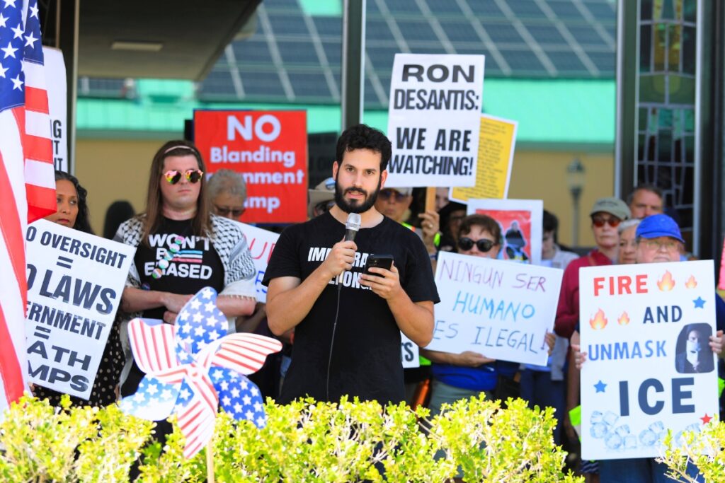 Gainesville Immigrant Neighbor Inclusion Initiative Coordinator Ethan Maia de Needell speaks at Camp Blanding ICE detention center rally. Photo by Seth Johnson