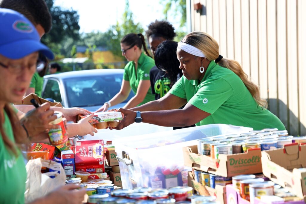Natasha Bass with Publix Serves takes a pack of applesauce from another associate to place in a bin at the Food4Kids warehouse in Gainesville on Tuesday. (Photo by Libby Clifton