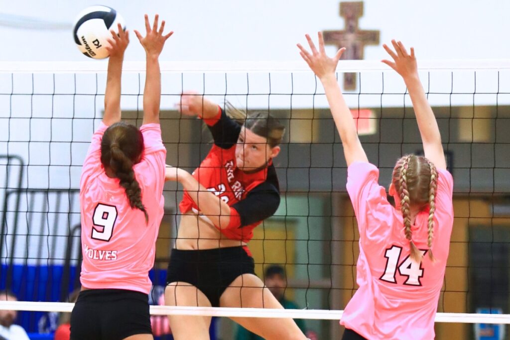 The Rock's Alexis Rhoden (23) with a hit against Saint Francis Catholic's Gianna Morali (9) and Hailey Schoster (14). Photo by C.J. Gish