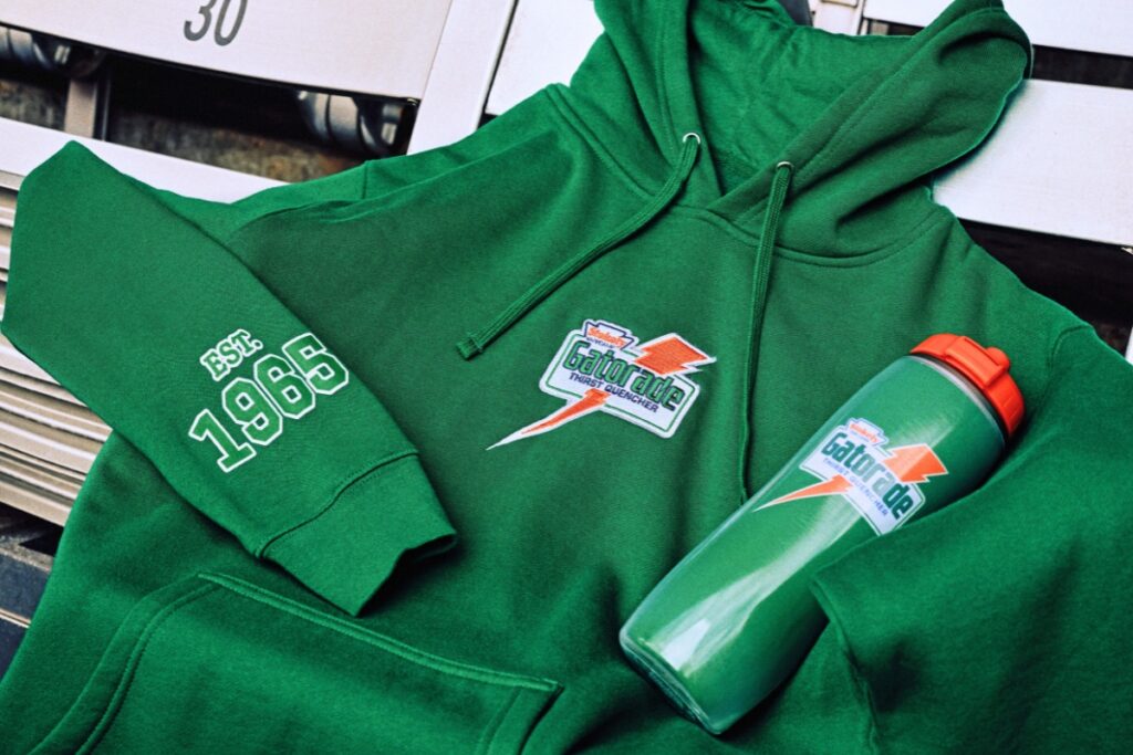 A cream crewneck with a Gatorade towel, and a green hoodie with a Gatorade squeeze bottle. Courtesy of Mitchell & Ness