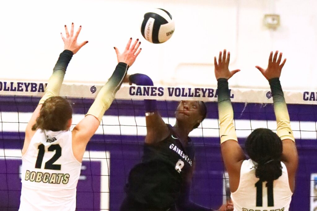 Gainesville's Jorryn Dye (8) with a hit against Buchholz's Taylor Sembower (12) and Demmi Strappy (11). Photo by C.J. Gish