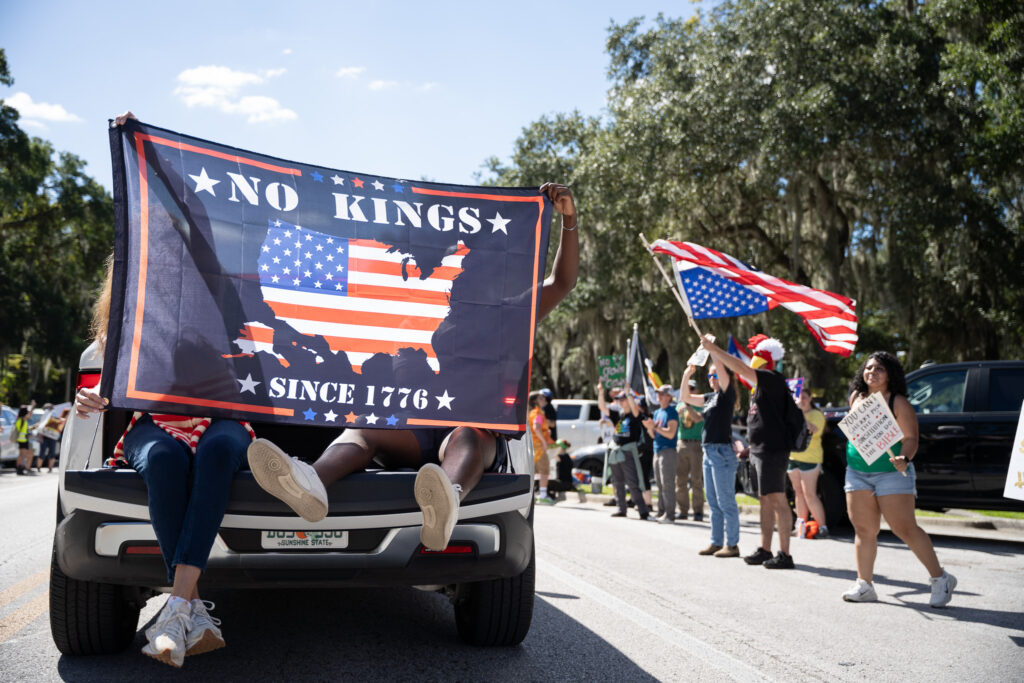 Protesters riding in the back of a vehicle with flags at the No Kings Gainesville Protest