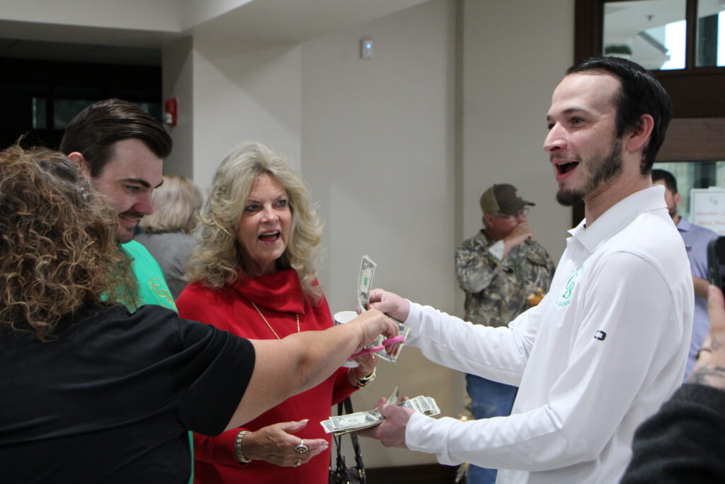 Kathy Putnam (center) receives a piece of the dollar bill ribbon celebrating Gala Banks Gainesville location grand opening. 