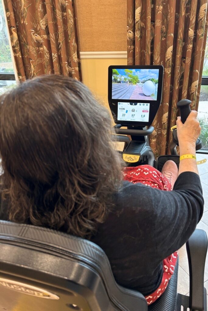The author rides a stationary exercise bike at Magnolia Ridge Rehabilitation Center on a ride that takes her through Singapore’s Marina Bay. Courtesy of Ronnie Lovler