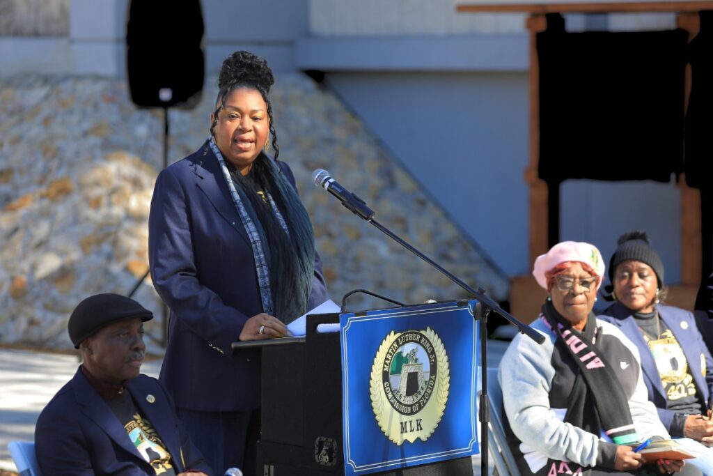 Diyonne McGraw speaks from behind a podium at Gainesville's MLK Jr. Memorial Gardens.
