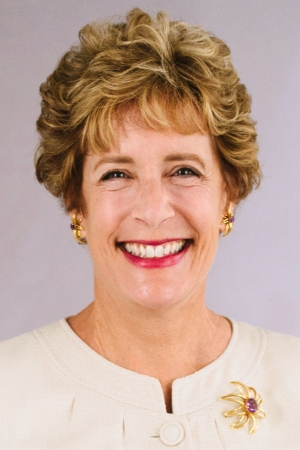 Liz Coursen. Photo of a woman in a white top and short curly hair.
