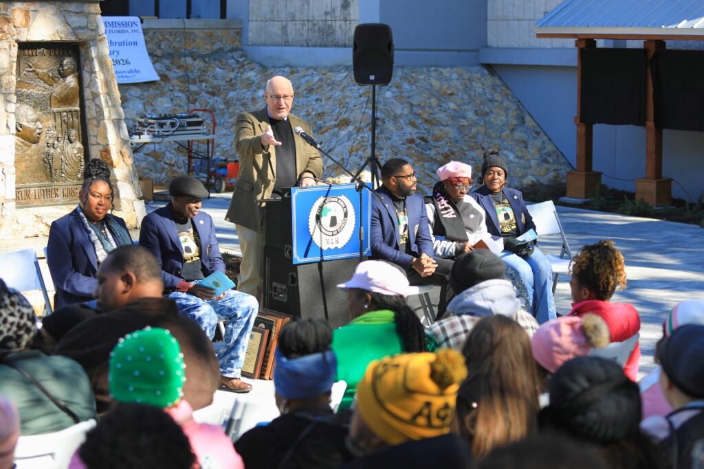 Mayor Harvey Ward speaks behind a podium with dignitaries to each side.