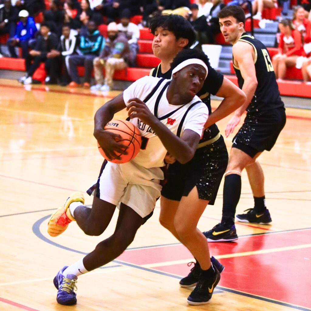Williston's Jac Edwards (0) drives to the basket against Buchholz's Ezra Olmedo (12). Photo by C.J. Gish