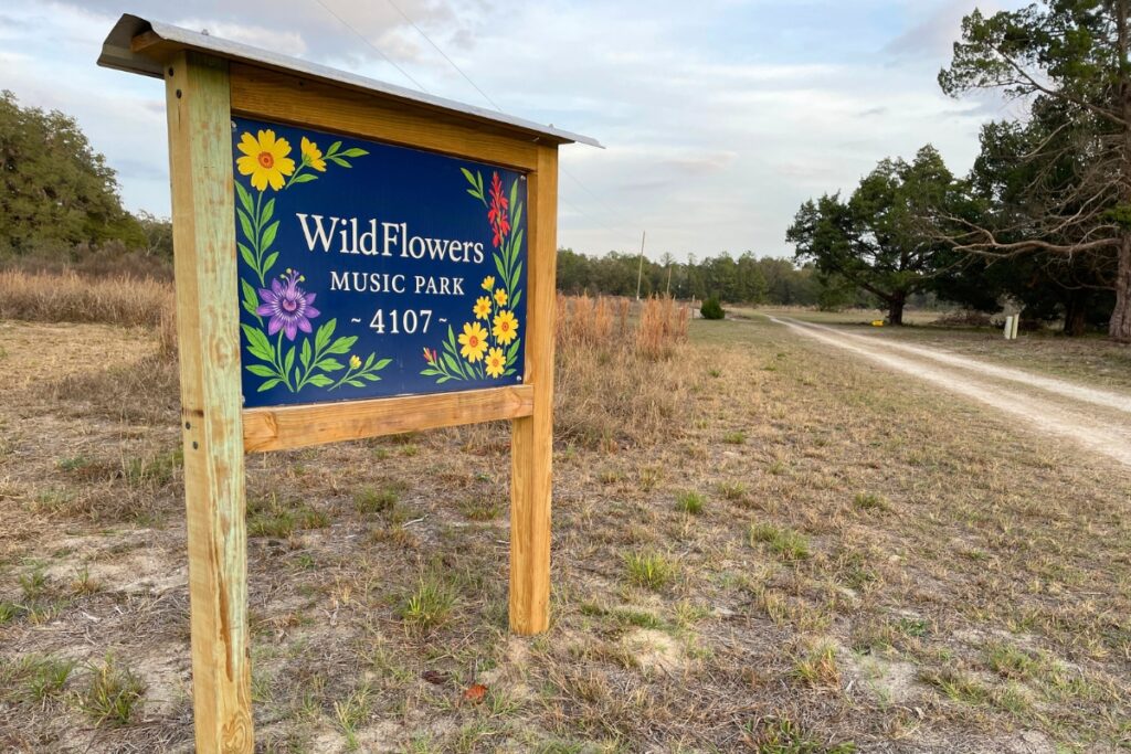The entrance to WildFlowers Music Park with a sign and long limestone road.