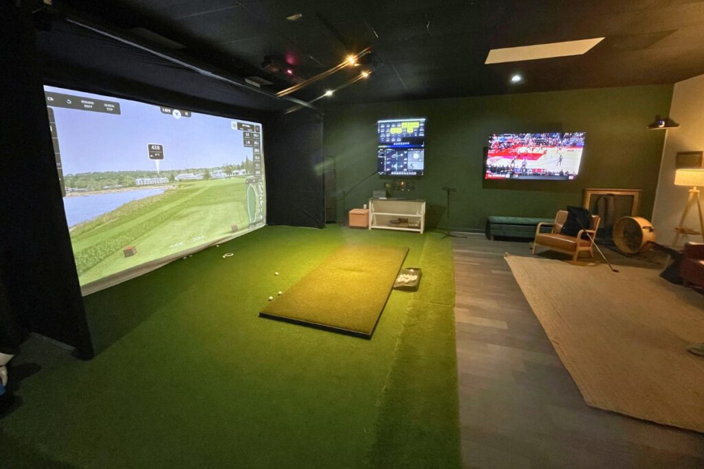 An indoor golf bay at Future Country Club with a simulator screen, turf and data screens.