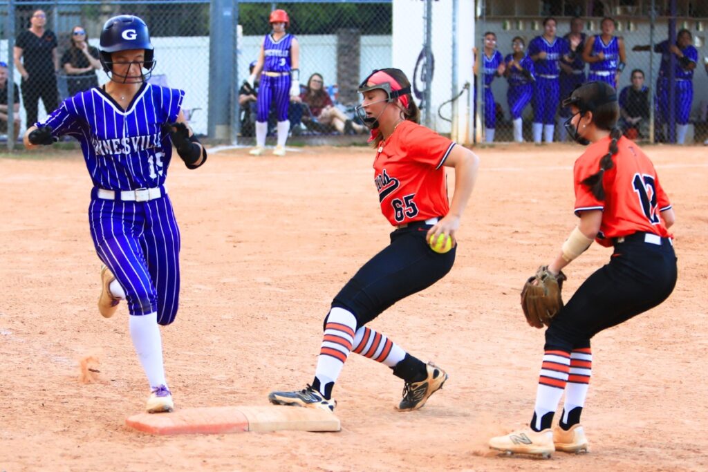 Gainesville's Lana Renicks (15) gets to first base safely in the first inning as Trenton's MacKenzie Fisher (65) also put her foot on the bag simultaneously. Photo by C.J. Gish